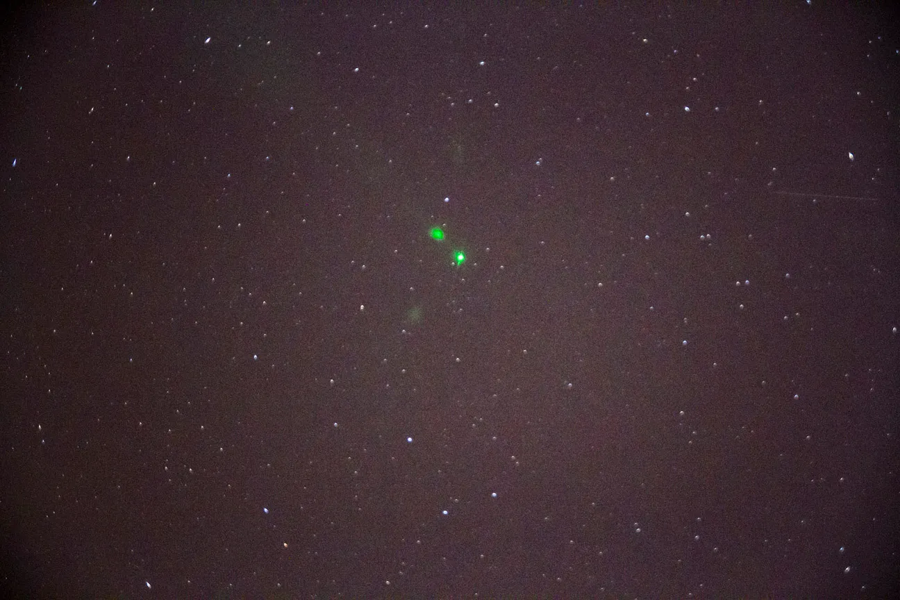 A dark starfield photographed from the ground, with bright green points near the center - the visible returns of CALIPSO's lidar.